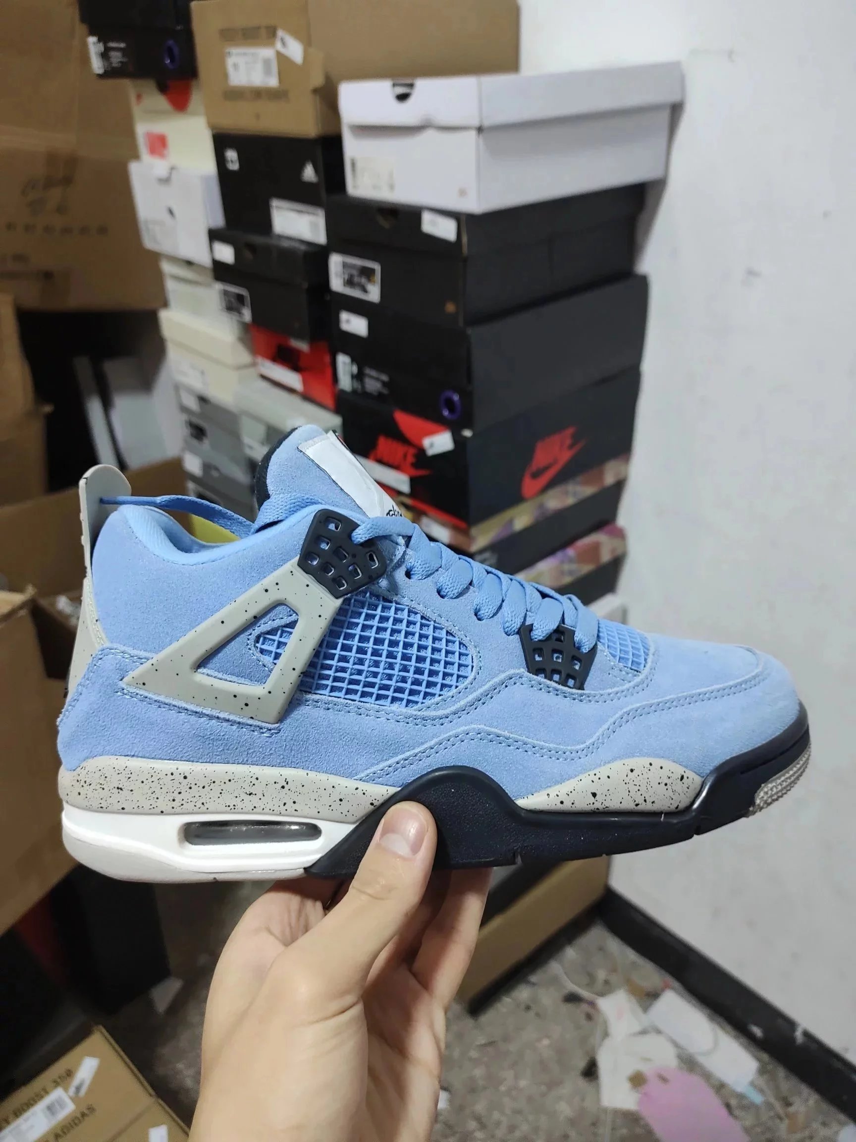 AJ4 University Blue — The Air Jordan 4 SE in University Blue features a classic North Carolina blue suede upper, accented with black lace locks and eye-catching gray splatter detailing that draws the eye. The logo on the tongue also differs from previous iterations.